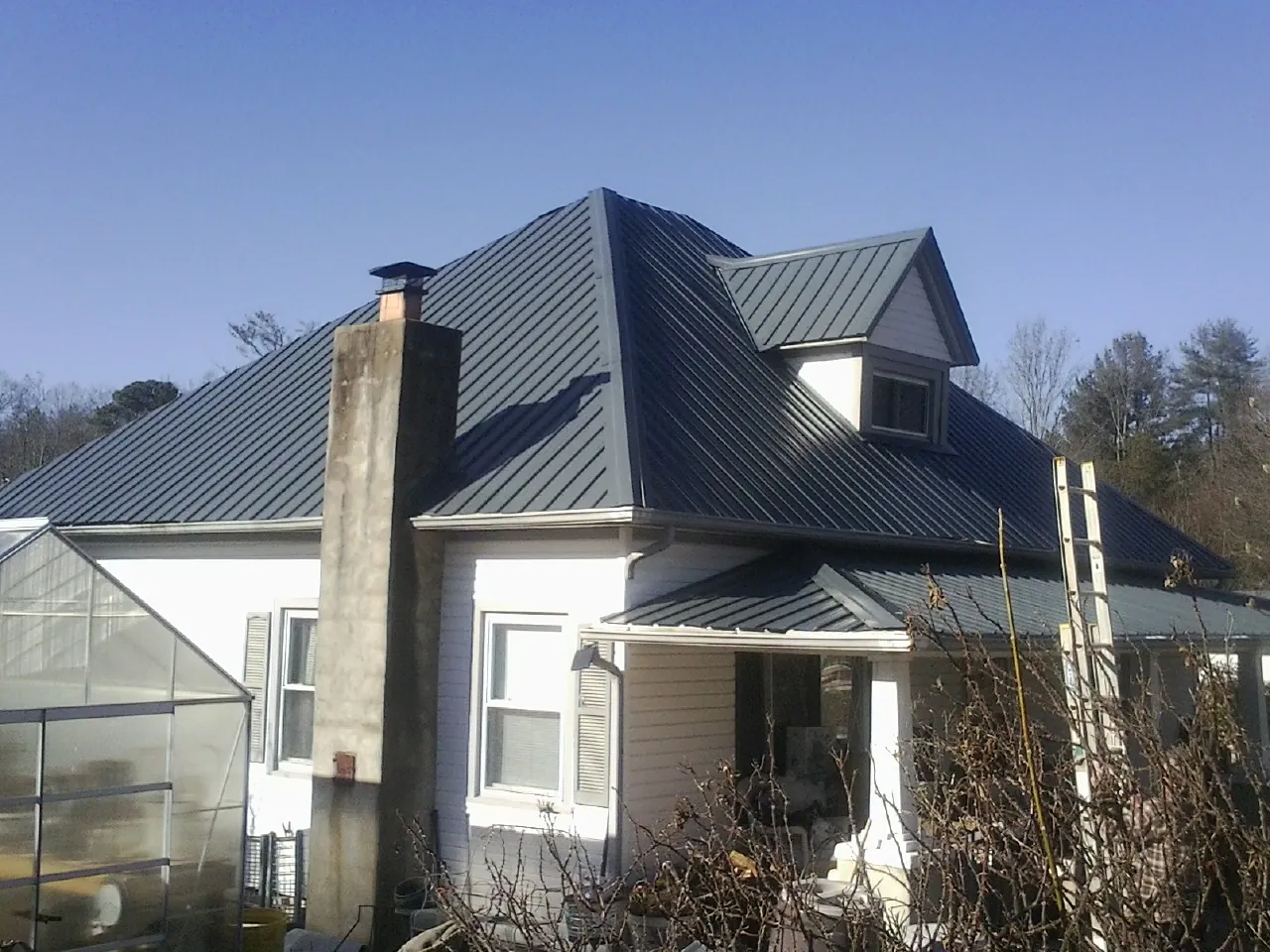 Dark blue standing seam metal roof on a white farmhouse with dormer — Slate & Tile Roof Repair by Roofing Brothers in Westdale