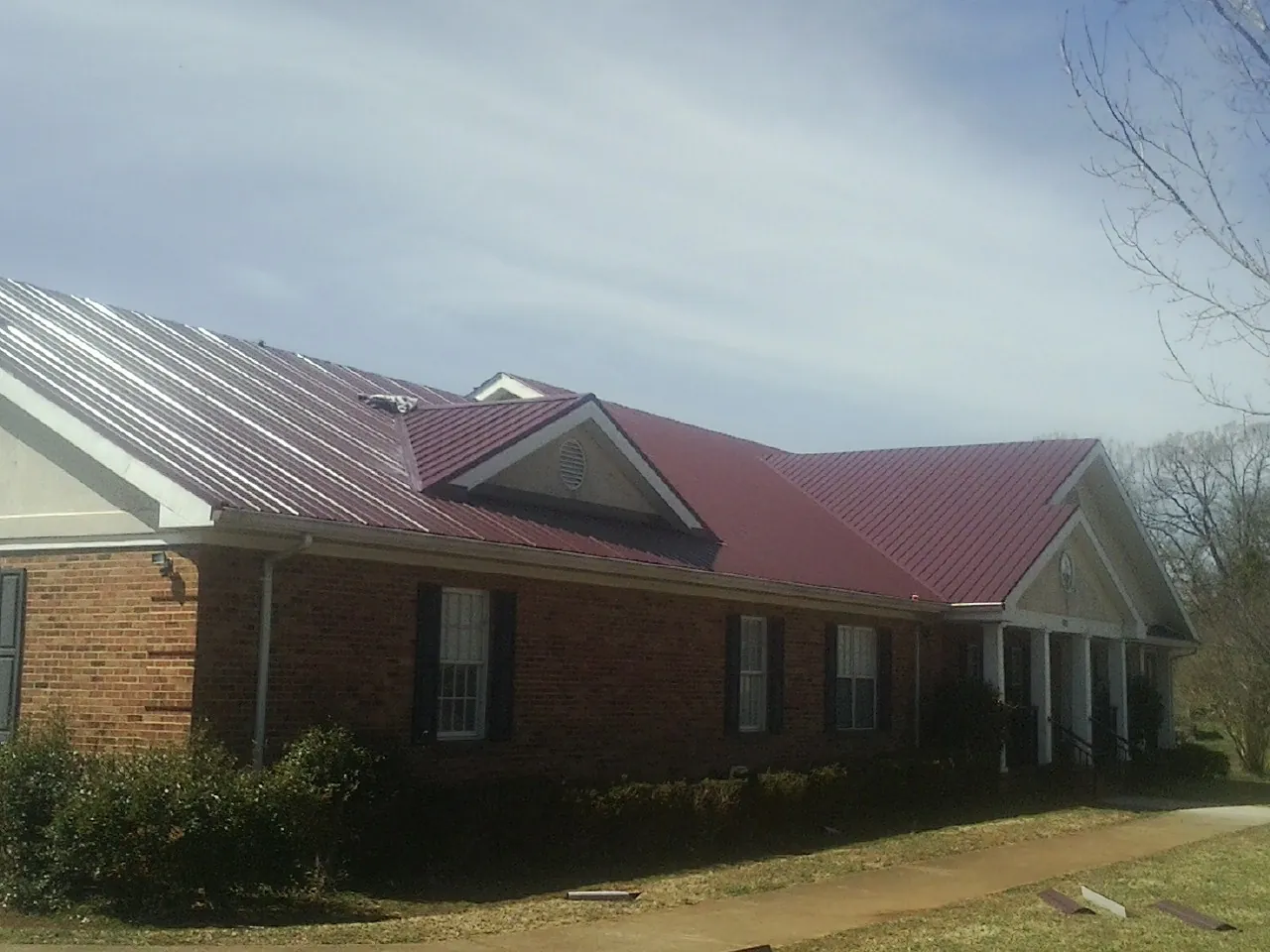 Red metal roof with gabled entries on a long brick building, from a Hail Damage Roof Repair job in Westdale
