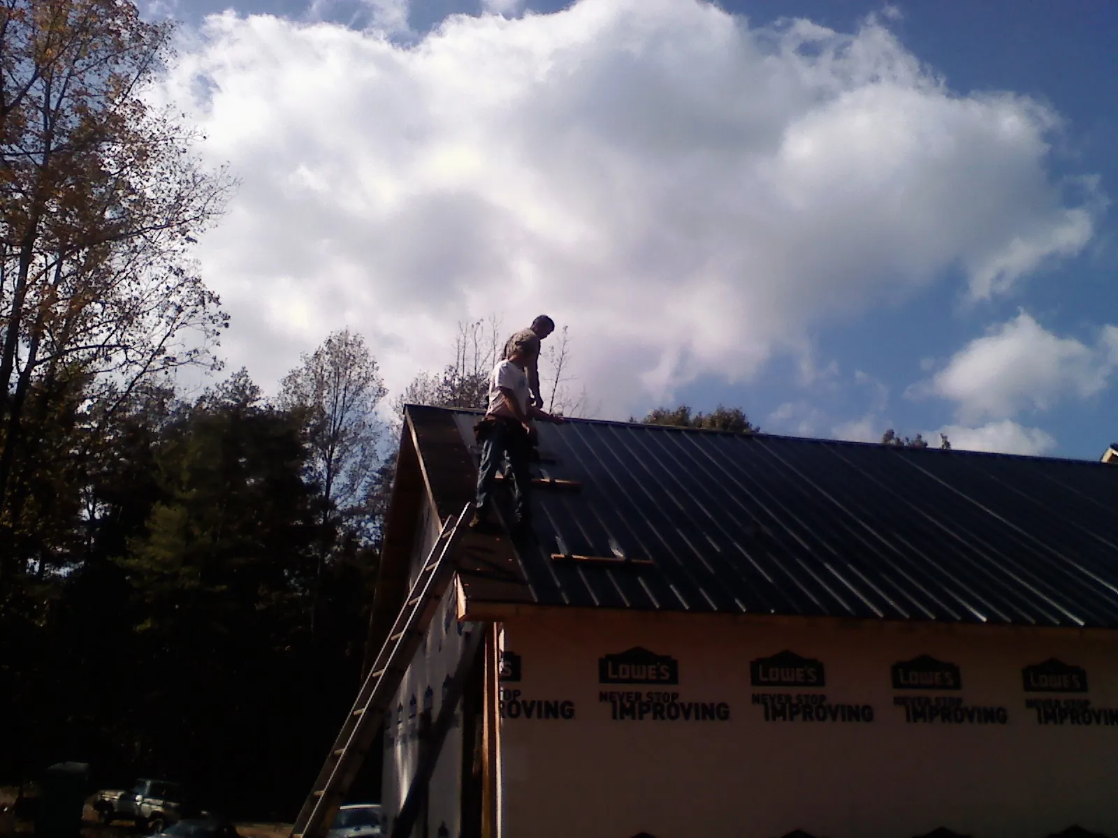 Roofer fastening dark metal panels high against a cloudy sky, from a Roof Inspection job in Westdale