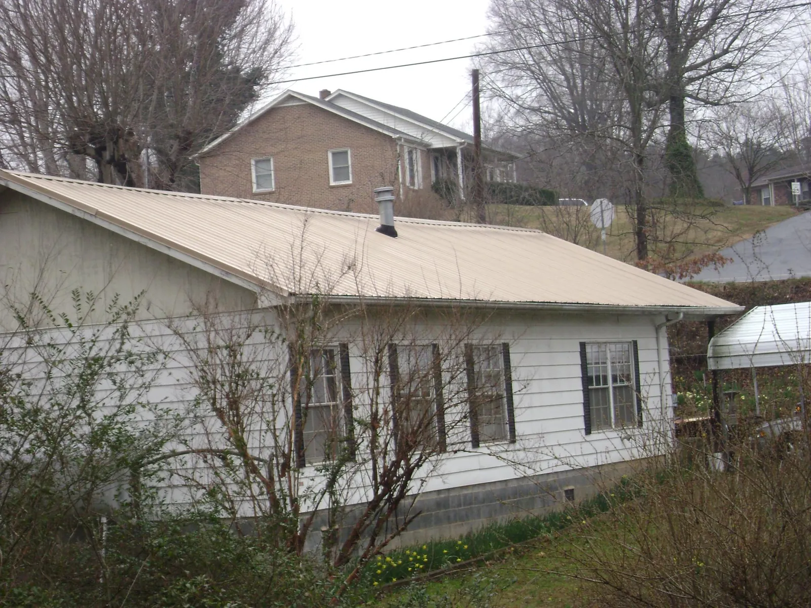 Tan metal roof on a white sided house set into a hillside — Commercial Roofing by Roofing Brothers in Westdale