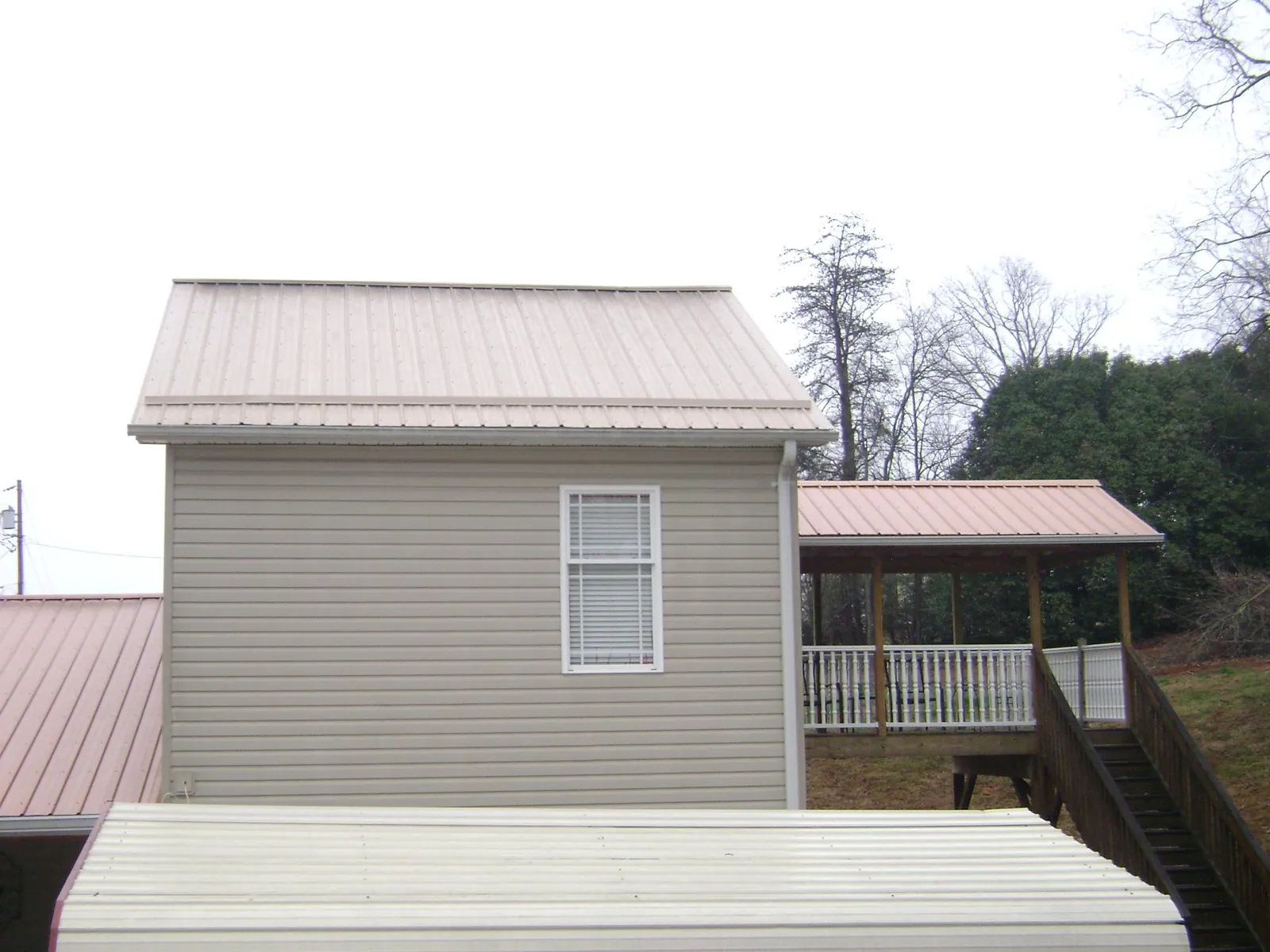 Tan metal roofs on a two story addition and attached porch, from a Roof Replacement job in Westdale